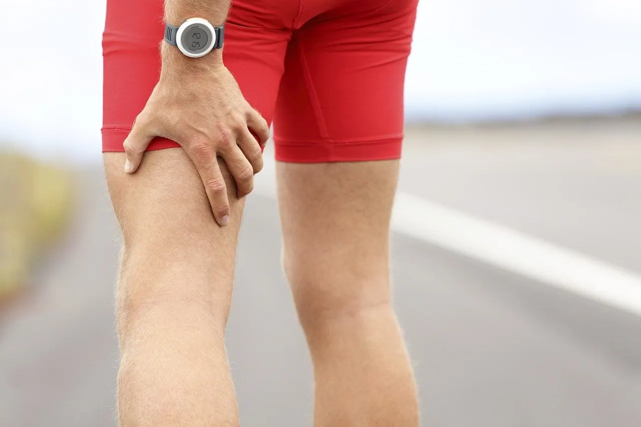 Läufer in roter Sporthose fasst sich mit einer Hand an den Oberschenkel, im Hintergrund eine unscharfe Landstraße