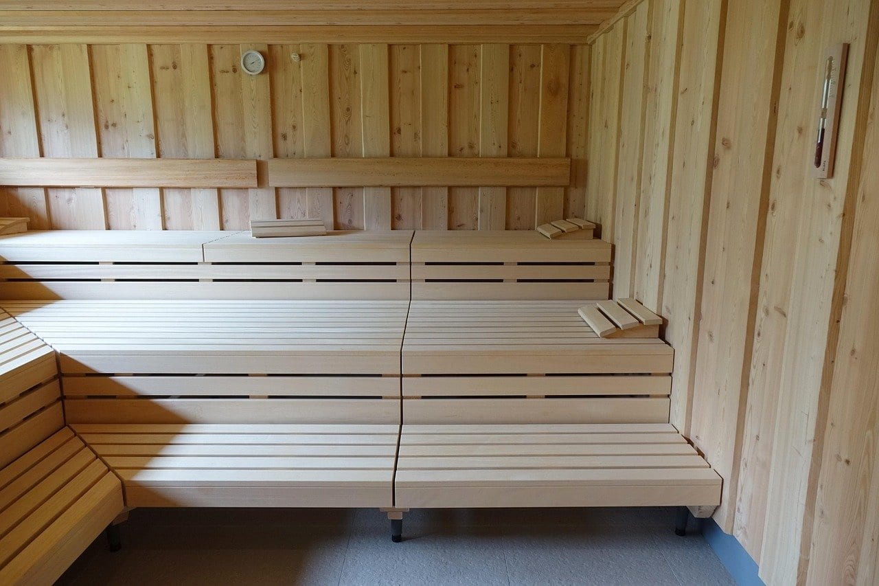 Saunakabine aus hellem Holz mit drei gestuften Bänken und hölzernen Kopfstützen, rechts an der Wand ein Thermometer
